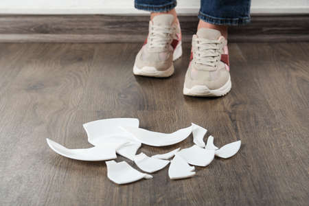 Woman in sneakers standing near broken plate on floor indoors, closeup