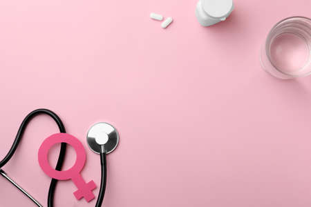 Female gender sign, stethoscope, pills and glass of water on pink background, flat lay. Space for textの写真素材