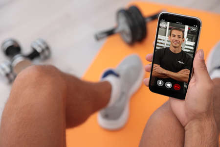 Man having workout with personal trainer via smartphone at home, closeupの写真素材