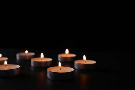 Burning candles on black background, space for text.