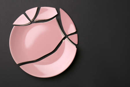 Pieces of broken pink ceramic plate on dark gray background, top view. Space for text