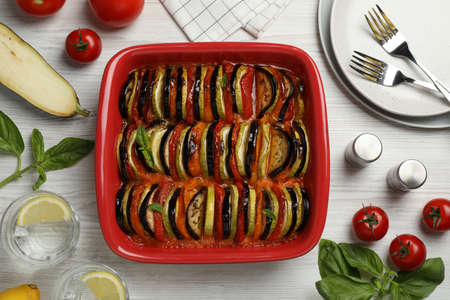 Delicious ratatouille in baking dish and ingredients on white wooden table, flat layの写真素材