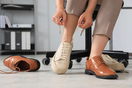 Woman taking off uncomfortable shoes and putting on sneakers in office, closeupの写真素材
