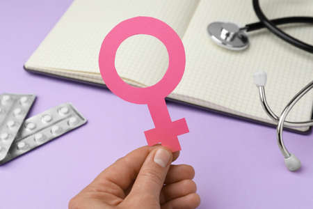 Girl holding female gender sign near open notebook, stethoscope and blisters of pills on violet background, closeup. Women's health conceptの写真素材