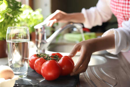 Woman with fresh tomatoes at countertop in kitchen, closeupの写真素材
