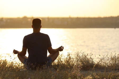 Man meditating on hill near river at sunset, back view. Space for textの写真素材