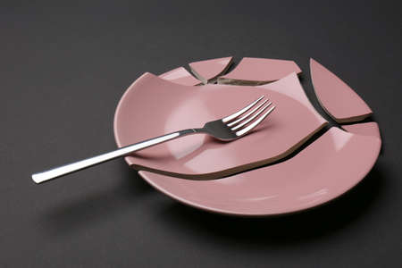Pieces of broken ceramic plate and fork on dark gray backgroundの写真素材