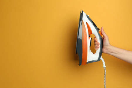 Woman holding modern iron on orange background, closeup. Space for text