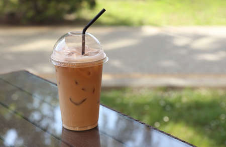 Plastic takeaway cup of delicious iced coffee on table in outdoor cafe, space for text