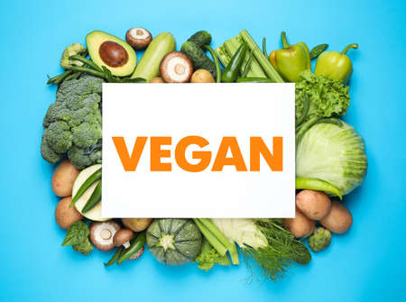 Paper card with word Vegan and fresh vegetables on turquoise background, flat layの写真素材