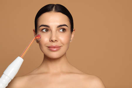Woman using high frequency darsonval device on beige background. Space for text