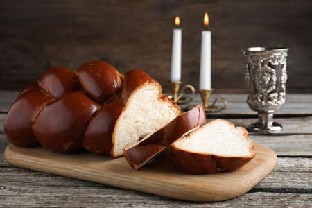 Cut homemade braided bread, goblet and candles on wooden table. Traditional Shabbat challahの写真素材