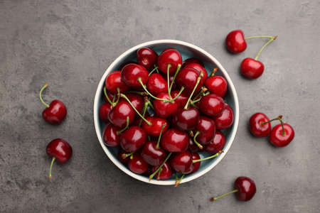 Bowl with ripe sweet cherries on gray table, flat lay