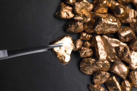 Tweezers with gold nugget above pile on black table, top view