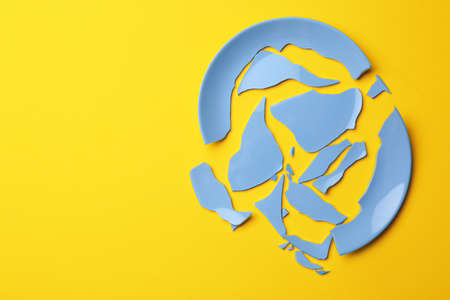 Pieces of broken light blue ceramic plate on yellow background, top view. Space for textの写真素材