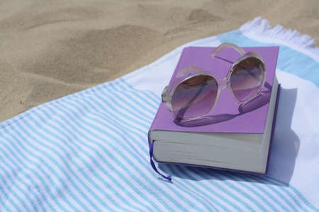 Beach towel with book and sunglasses on sand, space for textの写真素材
