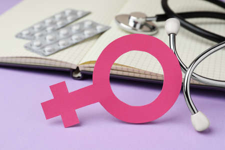 Female gender sign near open notebook, stethoscope and blisters of pills on violet background, closeup. Women's health conceptの写真素材