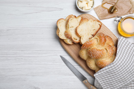 Cut freshly baked braided bread, honey and butter on white wooden table, flat lay with space for...