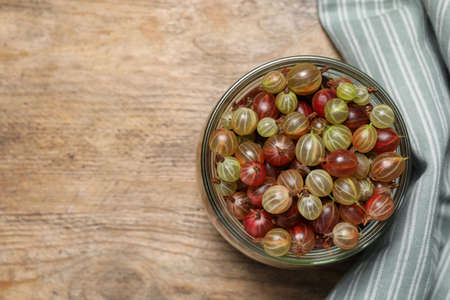 Jar of fresh ripe gooseberries on wooden table, top view. Space for textの写真素材