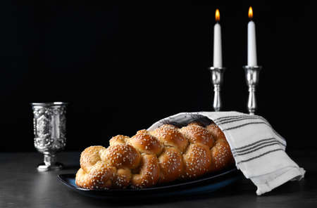 Homemade braided bread with sesame seeds, goblet and candles on dark gray table. Traditional Shabbat challahの写真素材