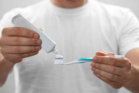 Man applying toothpaste on brush against gray background, closeup