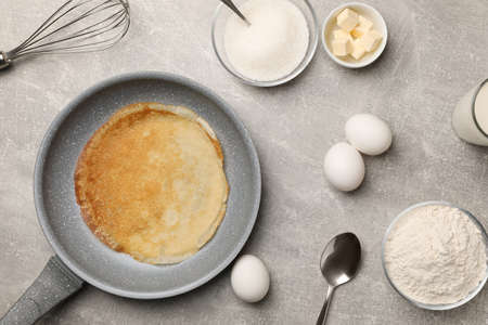 Frying pan with delicious crepe and ingredients on gray table, flat layの写真素材