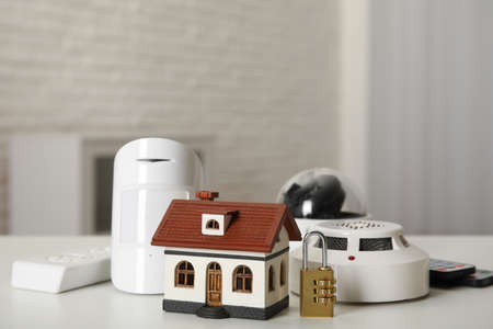 House model, CCTV camera, remote control, lock, smoke and movement detectors on table in room. home...