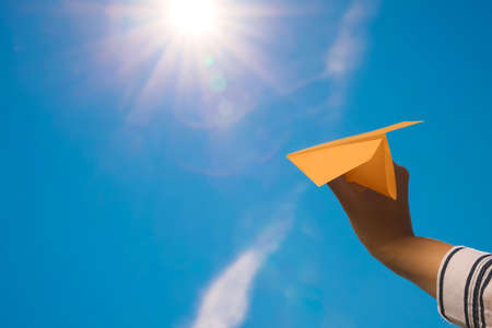 Woman holding orange paper plane against blue sky, closeup. Space for textの写真素材