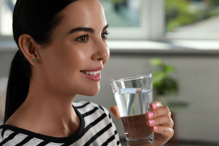 Young woman with glass of water indoors, closeup. Refreshing drinks
