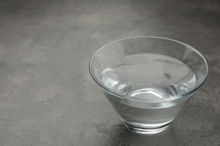 Glass bowl with water on gray table. Space for text