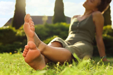 Woman sitting barefoot on green grass outdoors, closeupの写真素材