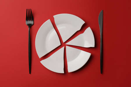 Pieces of broken ceramic plate and cutlery on red background, flat layの写真素材