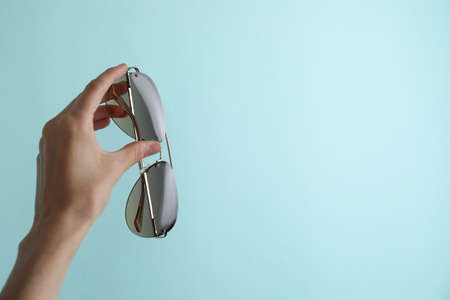 Woman holding stylish sunglasses on light blue background, closeup. Space for text