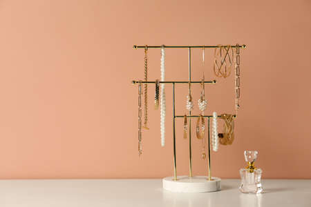 Holder with set of luxurious jewelry and perfume on white table near pale pink wall, space for textの写真素材