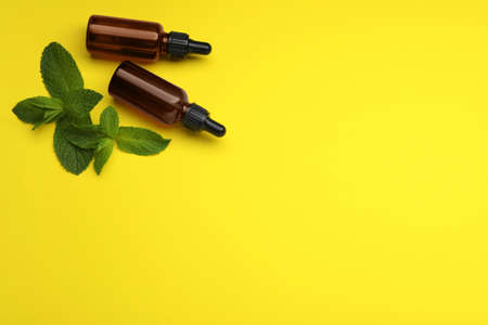 Bottles of essential oil and mint on yellow background, flat lay. Space for textの写真素材