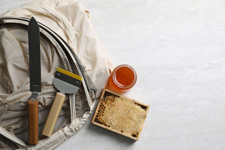 Different beekeeping tools and jar of honey on white table, flat lay. Space for text