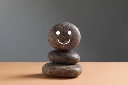 Stack of stones with drawn happy face on beige table against gray background. Zen conceptの写真素材