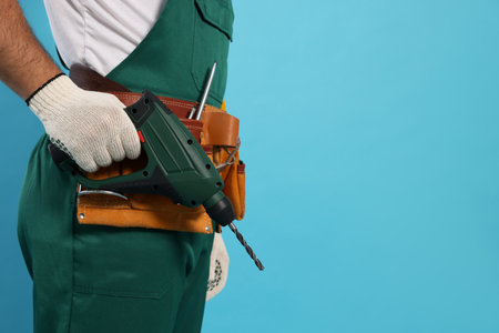 Worker in uniform with power drill on light blue background, closeup. Space for textの写真素材