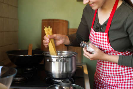 Woman cooking spaghetti on stove in kitchen, closeupの写真素材
