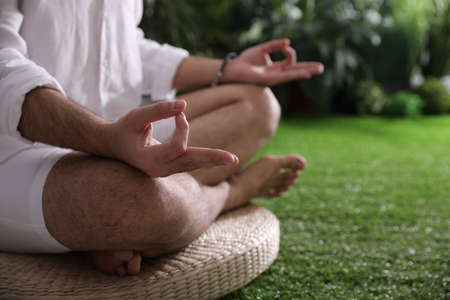 Young man meditating on straw cushion outdoors, closeup. Space for textの写真素材