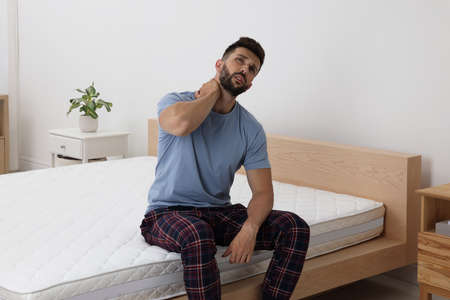 Man suffering from neck pain after sleeping on uncomfortable mattress at homeの写真素材