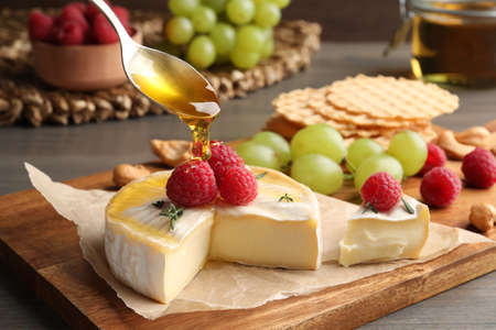 Pouring honey onto brie cheese served with raspberries on table, closeupの写真素材