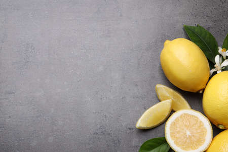 Many fresh ripe lemons with green leaves and flowers on gray table, flat lay. Space for textの写真素材