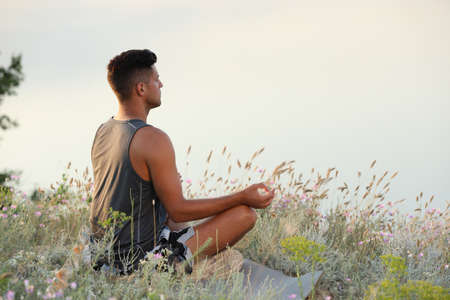 Man meditating in meadow near river. Space for text