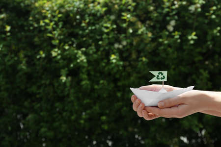 Woman holding paper boat with recycling symbol outdoors, closeup. Space for textの写真素材