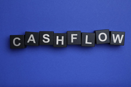 Black wooden cubes with phrase Cash FLow on blue background, flat layの写真素材