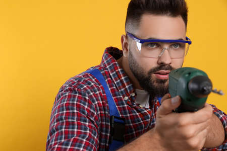 Young worker in uniform with power drill on yellow backgroundの写真素材