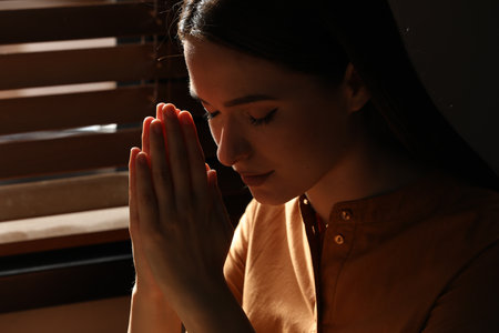 Religious young woman with clasped hands praying indoors, closeupの写真素材