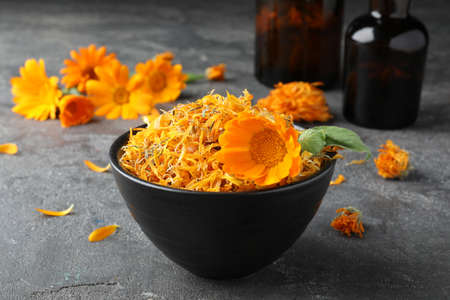 Bowl of dry and fresh calendula flowers on gray tableの写真素材