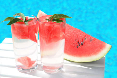 Refreshing drink in glasses and sliced watermelon near swimming pool outdoors